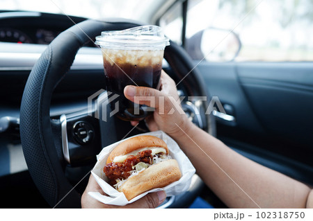 Asian woman driver hold and eat hamburger in car, dangerous and risk an accident. Asian woman driver hold and eat hamburger in car, dangerous and risk an accident. 102318750