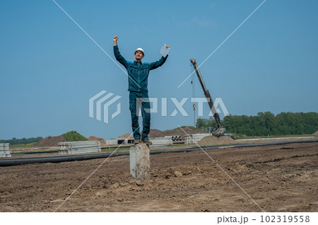 Builder in a protective helmet holds a laptop and stands on a pile in the middle of a construction site.  102319558