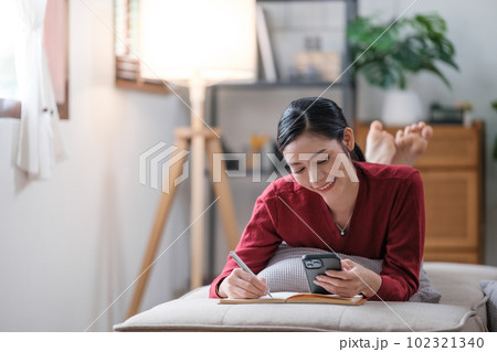 Asian woman woman reading book sitting on sofa in living room. 102321340