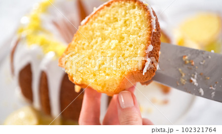 Step by step. Slicing lemon bundt cake decorated with lemon zest on a cake stand. 102321764