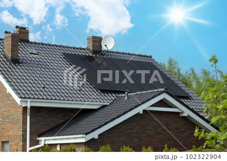 Modern house, dark solar panels, sunlit sky. Roof and photovoltaic technology. Modern house, dark solar panels, sunlit sky. Roof and photovoltaic technology. 102322904