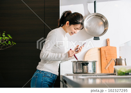 スマホを見ながら料理する女性 スマホを見ながら料理する女性 102327295
