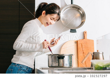 スマホを見ながら料理する女性 102327297