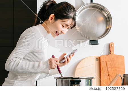 スマホを見ながら料理する女性 スマホを見ながら料理する女性 102327299