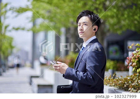 ビジネス街でイヤホンを着けて通話する若い日本人男性 ビジネス街でイヤホンを着けて通話する若い日本人男性 102327999