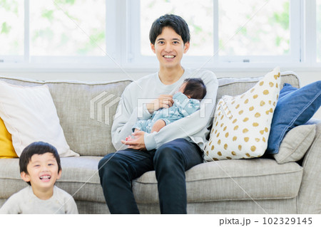 ソファーで赤ちゃんを抱っこするお父さん ソファーで赤ちゃんを抱っこするお父さん 102329145