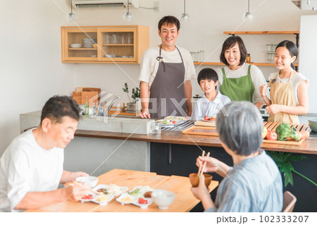 家のダイニングで祖父母に料理を作る孫・親子（二世帯住宅） 102333207