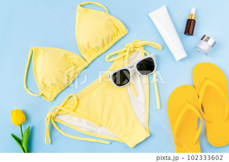Top view of bikini and cream bottle, sandals, sunglasses with beach accessories. 102333602