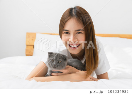 Young Asian woman lying on bed and playing small Scottish kitten on the room. Young Asian woman lying on bed and playing small Scottish kitten on the room. 102334983