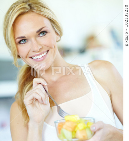 Fresh fruit salad is the best. Attractive young blonde woman enjoying a delicious fresh fruit salad at home. 102335230