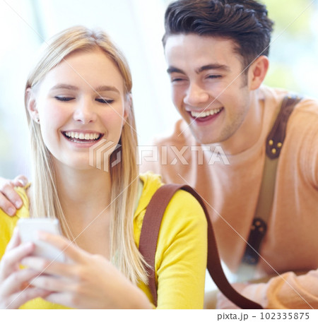 Laughing at the phone together. Young teen couple reading texts on a cellphone. 102335875