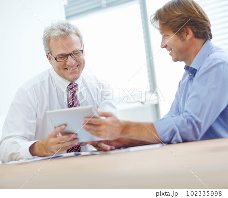 Strategies are looking positive. Two male colleagues expressing positivity and looking over the contents of a tablet. 102335998