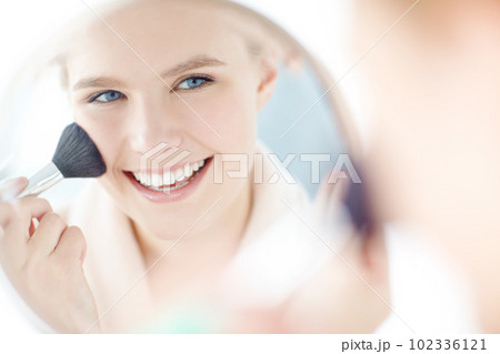 Adding a blush to her cheeks. a reflection of a woman applying her blush in the mirror. Adding a blush to her cheeks. a reflection of a woman applying her blush in the mirror. 102336121