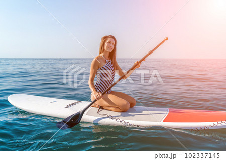 Woman summer surfing on the beach: A sporty girl in a striped swimsuit rides the waves on a surfboard on a sunny summer day at the beach, enjoying the fun and excitement of surfing. Woman summer surfing on the beach: A sporty girl in a striped swimsuit rides the waves on a surfboard on a sunny summer day at the beach, enjoying the fun and excitement of surfing. 102337145