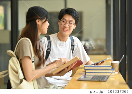 Two happy students sitting in coffee shop learning and preparing for exams. Education and youth lifestyle concept 102337365