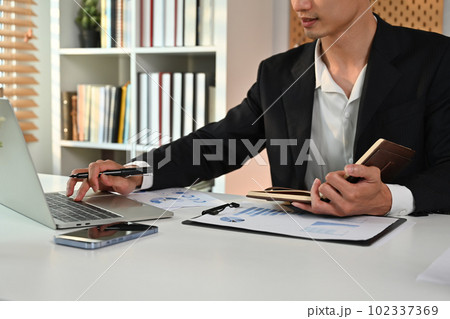 Male economist in black suit preparing report and analyzing work results at workstation 102337369