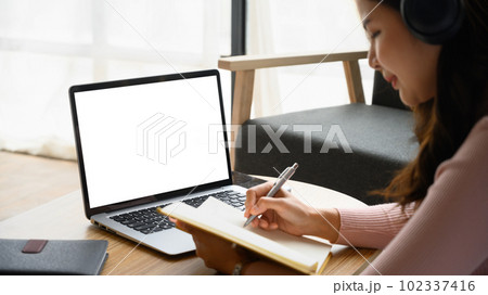 Concentrated young woman having distance learning online virtual class on laptop and making notes on notebook Concentrated young woman having distance learning online virtual class on laptop and making notes on notebook 102337416