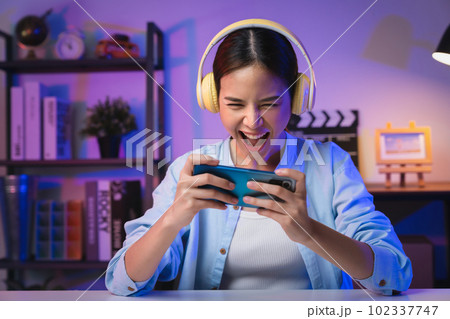 woman wearing headset and playing online game on smartphone with live broadcasting on internet. woman wearing headset and playing online game on smartphone with live broadcasting on internet. 102337747