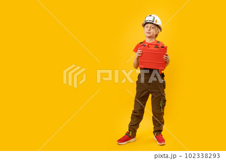 Full-length portrait of boy imitating worker. Child wears helmet with holds toolbox, isolation on yellow background. Copy space, mock up Full-length portrait of boy imitating worker. Child wears helmet with holds toolbox, isolation on yellow background. Copy space, mock up 102338293