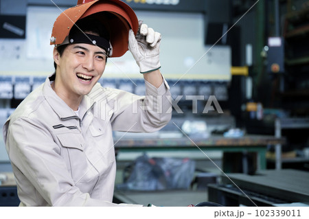 アーク溶接などで使うマスクを持つ作業着を着た笑顔の男性	 102339011