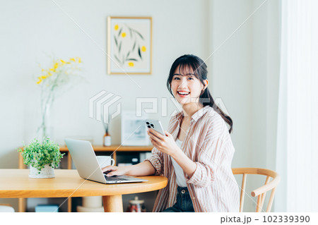 家でパソコンとスマホを使う若い女性 102339390