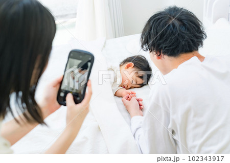 赤ちゃんの寝顔をスマホで撮影するパパとママ 赤ちゃんの寝顔をスマホで撮影するパパとママ 102343917