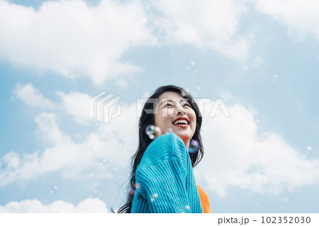 楽しげに笑顔でシャボン玉をみつめる若い女性 102352030