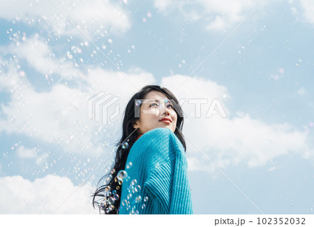 青空の下笑顔でシャボン玉を見つめる若い女性 青空の下笑顔でシャボン玉を見つめる若い女性 102352032