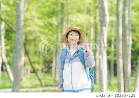 新緑の中でハイキングするシニア女性の写真 102357229