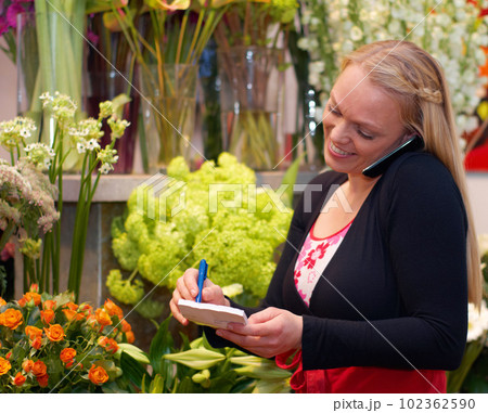 Small business, woman on phone call and in florist writing an order. Flowers or plants, communication or customer service and female worker with smartphone or cellphone with client for a bouquet 102362590