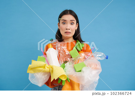 Young confused asian girl with different types of plastic, learns how to recycle, saving enviroment, sorting garbage, blue background 102366724