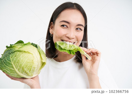 Close up of cute korean woman, eating cabbage, on diet, holding lettuce, isolated on white background Close up of cute korean woman, eating cabbage, on diet, holding lettuce, isolated on white background 102366756