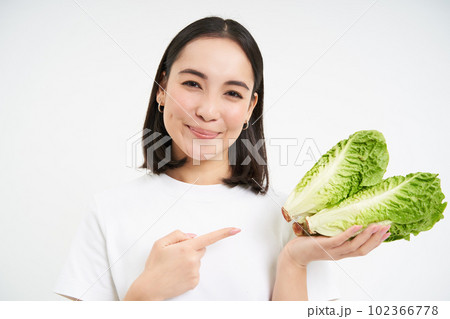 Smiling asian woman, pointing finger at cabbage, grew fresh vegetable, looks happy, isolated on white background 102366778