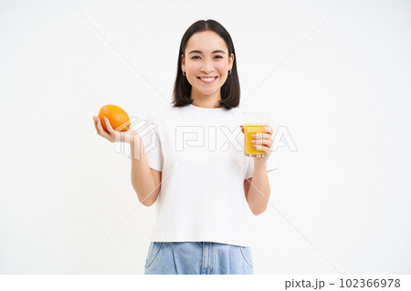 Beautiful and healthy young woman, starts her day with fresh juice, holding orange fruit and smiling, white background Beautiful and healthy young woman, starts her day with fresh juice, holding orange fruit and smiling, white background 102366978