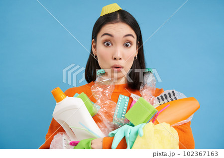 Portrait of asian woman with surprised face, holds plastic empty bottles and garbage for recycling, sorting stations, blue background Portrait of asian woman with surprised face, holds plastic empty bottles and garbage for recycling, sorting stations, blue background 102367163