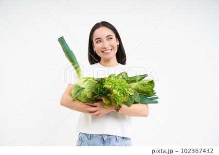 Portrait of happy young woman on green diet, likes eating organic food, holding fresh vegetables from garden, lettuce, cabbage, white studio background Portrait of happy young woman on green diet, likes eating organic food, holding fresh vegetables from garden, lettuce, cabbage, white studio background 102367432