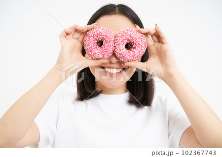 Image of funny young woman, makes glasses with two pink glazed doughnuts, looking through donnut holes and smiling, isolated on white background Image of funny young woman, makes glasses with two pink glazed doughnuts, looking through donnut holes and smiling, isolated on white background 102367743