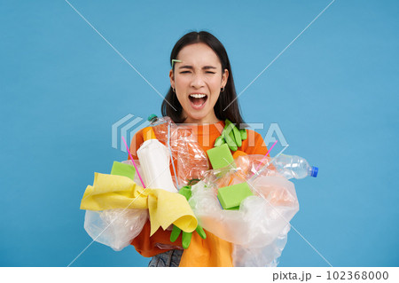Shocked eco activist, collects loads of plastic to recycle, looking upset at bottles and unsorted garbage, blue background Shocked eco activist, collects loads of plastic to recycle, looking upset at bottles and unsorted garbage, blue background 102368000