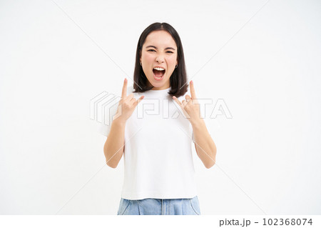 Excited asian woman, shows rock on, heavy metal horns gesture, having fun, enjoying concert or festival, white background 102368074