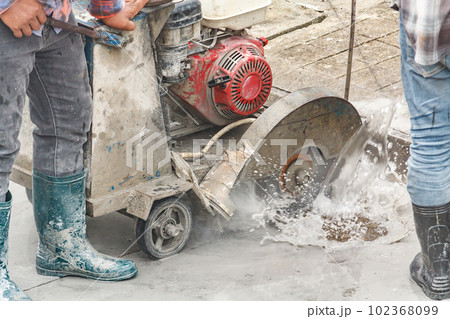 Worker using diamond saw blade machine cutting concrete road at construction site 102368099
