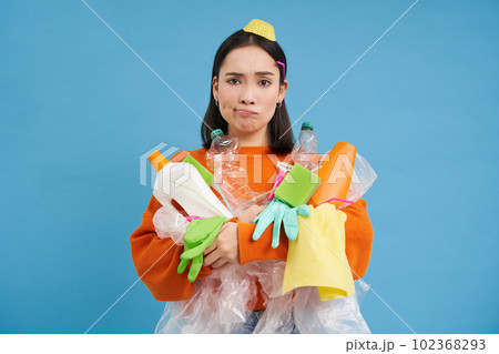 Complicated girl with garbage on her face, plastic empty bottles and waste, looking troubled and sad, blue background Complicated girl with garbage on her face, plastic empty bottles and waste, looking troubled and sad, blue background 102368293