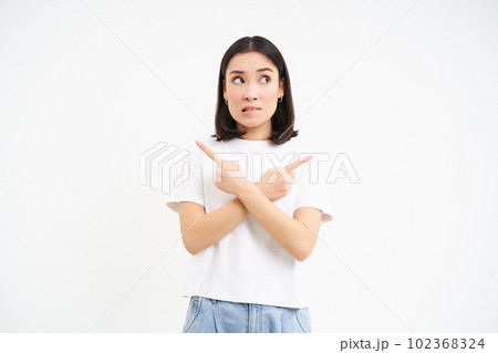 Thinking asian girl makes her decision, points sideways, two ways, choosing, stands isolated on white background 102368324