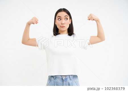 Portrait of young asian woman, flexing muscles, showing biceps and smiling with confidence, looking strong, standing over white background 102368379