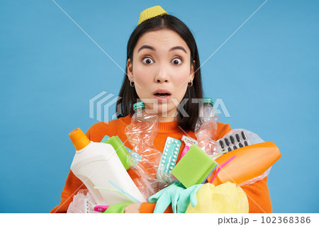 Portrait of girl with shocked face, holds empty plastic bottles, household garbage, stares startled at camera, recycles, blue background Portrait of girl with shocked face, holds empty plastic bottles, household garbage, stares startled at camera, recycles, blue background 102368386