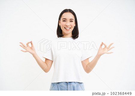 Peaceful smiling asian woman, standing calm and relaxed, holds hands in zen, meditation pose, isolated over white background 102368449