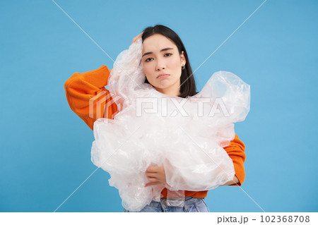 Young asian woman with plastic waste, looking bothered by recycling, standing over blue background Young asian woman with plastic waste, looking bothered by recycling, standing over blue background 102368708