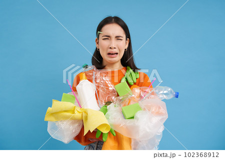 Sad asian female student, holds recycling waste, collects plastic garbage to take it to recycle center, blue background Sad asian female student, holds recycling waste, collects plastic garbage to take it to recycle center, blue background 102368912