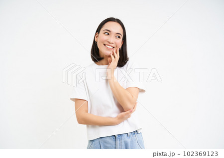 Portrait of tender, cute young asian woman, looking with flirty, silly ace expression, standing over white background 102369123