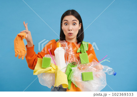 Asian woman looks shocked, holds plastic rubbish, sorting garbage for recycling, looks surprised, blue background Asian woman looks shocked, holds plastic rubbish, sorting garbage for recycling, looks surprised, blue background 102369333