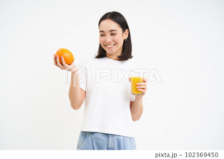 Beautiful and healthy young woman, starts her day with fresh juice, holding orange fruit and smiling, white background Beautiful and healthy young woman, starts her day with fresh juice, holding orange fruit and smiling, white background 102369450